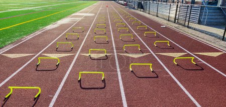 Photo for Four rows of yellow six inch mini hurdles set up in lanes on a track for runners to run over performing the wicket drill. - Royalty Free Image