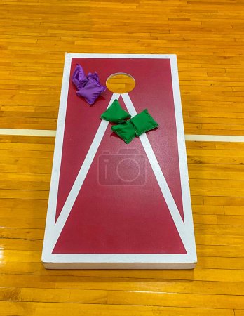 Maisloch-Spiel mit bunten Bohnensäcken im Inneren auf einem Turnhallenboden, der für High School Turnhalle Klasse verwendet wird.