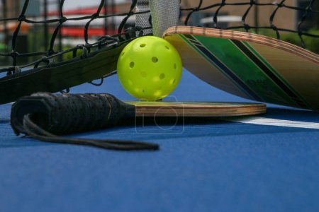 Foto de Primer plano de dos paletas de pickleball y bolas de whiffle debajo de una red en una cancha de pickleball de tenis. - Imagen libre de derechos