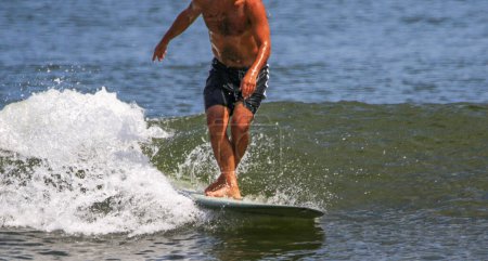 Photo for Man with no shirt surfing with his legs crossed while walking up his board riding a wave on a sunny day at the beach. - Royalty Free Image