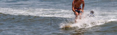 Photo for One man surfing and splashing on a small wave wearing  a colorful bathing suit and no shirt with copy space on the left. - Royalty Free Image