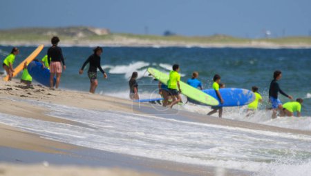 Photo for Gilgo Beach, New York, USA - 25 July 2023: Kids in neon green shirts walking into the ocean to go surfing at the Bunger Surf Camp at Gilgo Beach on Long Island. - Royalty Free Image