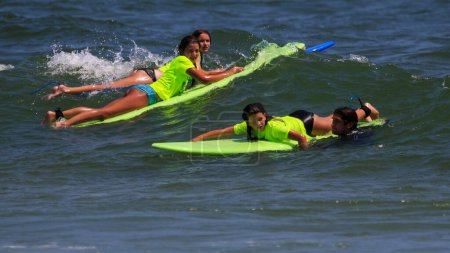 Photo for Gilgo Beach, New York, USA - 25 July 2023: Kids in neon green shirts riding on waves while surfing at Bunger Surf Camp at Gilgo Beach on Long Island. - Royalty Free Image
