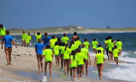 Photo for Gilgo Beach, New York, USA - 25 July 2023: Kids in neon green shirts walking down the beach to go surfing during the Bunger Surf Camp at Gilgo Beach on Long Island. - Royalty Free Image