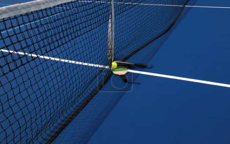 Foto de Dos paletas de pickleball con una bola de whiffle en la red en una cancha de pickleball azul. - Imagen libre de derechos