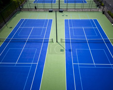 A drone view looking down at blue tennis pickleball courts lined with light blue for pickleball with lights.