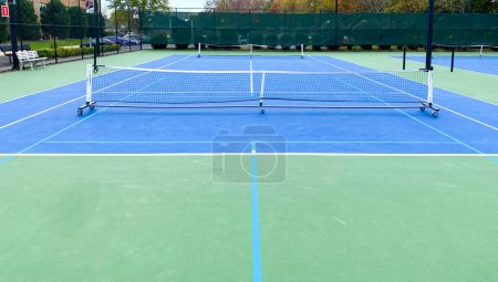 Zwei tragbare Pickleball-Netze auf einem Tennisplatz, die Platz für zwei Spiele machen, die gespielt werden können.