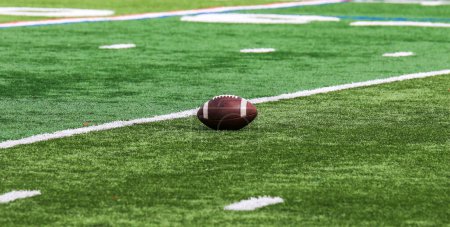 Téléchargez les photos : Un football américain reposant sur un terrain de gazon vert avec de la place pour la copie. - en image libre de droit