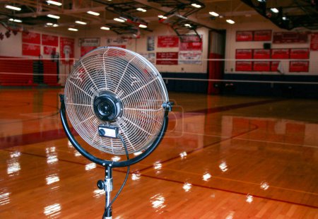Photo for A fan trying to cool off a gymnasium during summer volleyball camp practice. - Royalty Free Image