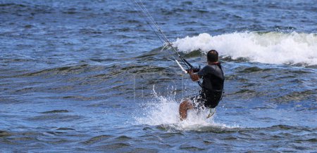 Photo for Rear view of a man splashing in the water while riding on a kiteboard not wearing a helmet. - Royalty Free Image