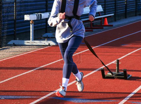 Close up of a front view of a female runner pulling a sled with weight on top.