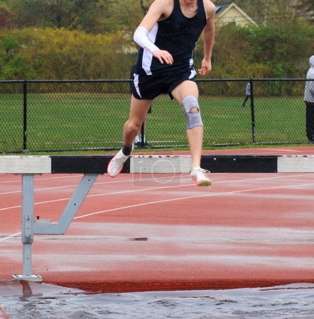 Foto de Un chico de secundaria corriendo la carrera en una pista se encuentra empujando la barrera sobre el agua. - Imagen libre de derechos