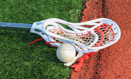 Lacrosse stick on the turf next to a ball close to a red track