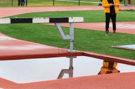 Reflection in the water of a track steeplechase water pit on a calm day.