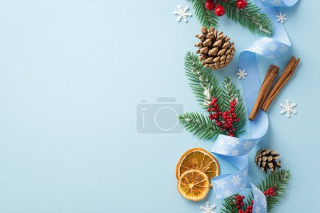Photo for Christmas concept. Top view photo of pine cones mistletoe berries fir branches curly ribbon dried orange slices cinnamon sticks and snowflake confetti on isolated pastel blue background with copyspace - Royalty Free Image