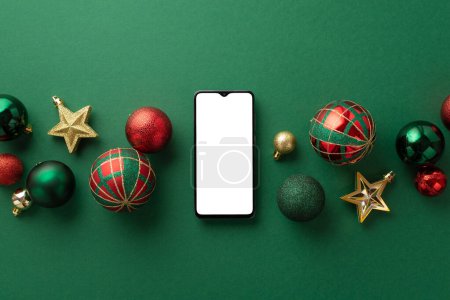 Téléchargez les photos : Concept de Noël. Vue du dessus photo de smartphone étoiles ornements or boules vertes et rouges sur fond vert isolé avec espace vide - en image libre de droit