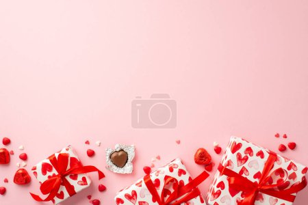 Photo for St Valentine's Day concept. Top view photo of gift boxes in wrapping paper with heart pattern chocolate candies and sprinkles on isolated light pink background with copyspace - Royalty Free Image