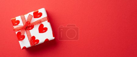 Téléchargez les photos : Valentine's Day concept. Top view photo of white giftbox in wrapping paper with heart pattern and ribbon bow on isolated red background with copyspace - en image libre de droit