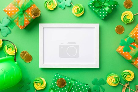 Saint Patrick's Day concept. Top view photo of empty photo frame gift boxes pot meringue lollipops gold coins and clovers on isolated green background with copyspace
