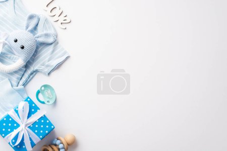 Téléchargez les photos : Concept de douche bébé. Vue du dessus photo de bleu vêtements pour bébés boîte cadeau tricoté lapin hochet jouet sucette et inscription amour sur fond blanc isolé avec copyspace - en image libre de droit