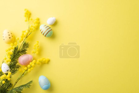 Easter concept. Top view photo of colorful easter eggs and bouquet of mimosa flowers on isolated yellow background with copyspace
