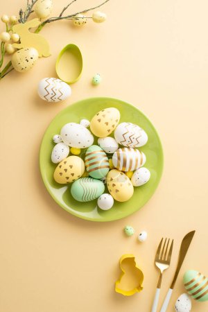 Easter atmosphere concept. Top view vertical photo of green plate with lot of colorful easter eggs cutlery baking molds and easter plant on isolated pastel beige background