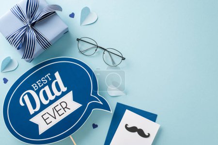 Photo for A top view flat lay for Father's Day with a greeting plaque, gift box, spectacles, paper hearts, envelope with postal on a pastel blue background with an empty space for text or advertisement - Royalty Free Image