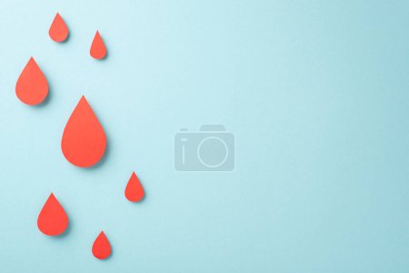 Photo for World Blood Donor Day theme. Overhead view image of blood droplets falling onto a pastel blue backdrop, with ample room for text or advertising - Royalty Free Image
