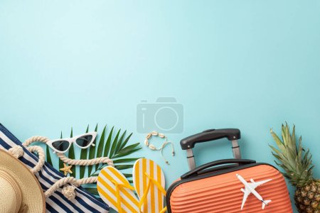 Summer holiday vibes! Top view of suitcase, mini plane figurine, beach accessories, glasses, sunhat, bag, flip-flops, shell bracelet, ananas, palm leaves, light blue backdrop, with empty space for ad