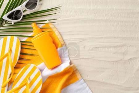 Téléchargez les photos : Concept de bronzage sain. Photo grand angle de pulvérisation de crème solaire, lunettes de soleil, pantoufles et feuille de palmier sur une serviette de plage sur fond de sable isolé avec copyspace - en image libre de droit