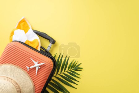 Foto de Sumérgete en la dicha del verano! Echa un vistazo a la maleta de vista superior, el avión en miniatura, los elementos esenciales de la playa como el sombrero de sol, la toalla y las hojas de palma sobre un fondo amarillo. Libera tu potencial publicitario de viajes en espacios abiertos - Imagen libre de derechos