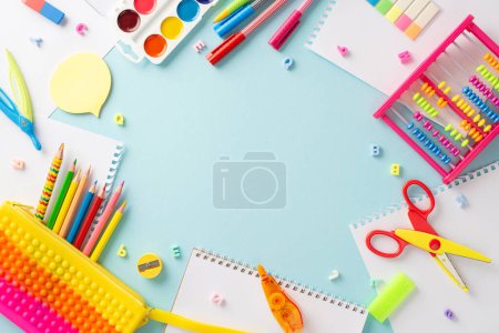 Entdecken Sie die Magie der Bildung für kleine Kinder durch dieses fesselnde Foto von oben: eine charmante Präsentation farbenfroher Schulmaterialien auf einem isolierten pastellblauen Hintergrund, bereit für Text oder Werbeaktionen