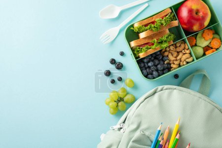 Ein verführerisches und gesundes Schulessen aus der Vogelperspektive. Lunchbox mit leckeren Sandwiches und Studentenrucksack auf blauer, isolierter Oberfläche, die Platz für Text oder Aktionen bietet