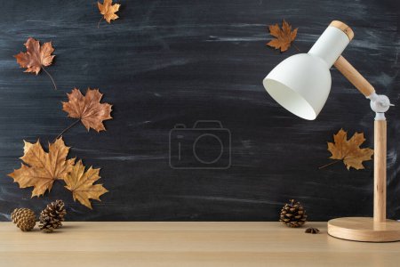 Photo for Dive into the excitement of new school term with this captivating side-view picture of wooden desk with lamp and maple leaves on chalkboard background. Personalize copy-space with text or promotions - Royalty Free Image