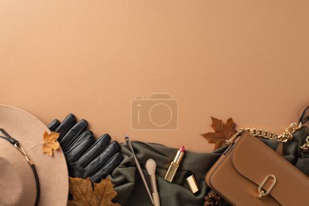 Téléchargez les photos : Concept de tenue féminine d'automne. Vue du dessus du bonnet en laine, gants en cuir, écharpe confortable, sac à main bronzé, rouge à lèvres, pinceaux cosmétiques, feuilles d'érable, cônes sur fond beige, espace pour le texte ou la publicité - en image libre de droit