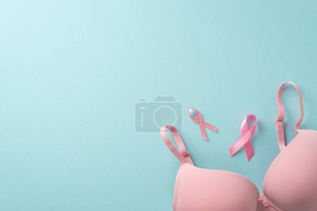 Concepto de lucha contra el cáncer de mama. Foto de vista superior de signos de cinta rosa y sujetador sobre fondo azul pastel con espacio en blanco para mensaje motivacional o promoción