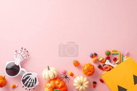 Elegant Halloween trick-or-treat concept. Top view showcasing thematic elements: mini pumpkins, bone, bag with candy corn, sweets, spider, party glasses on light pink backdrop. Room for greeting or ad