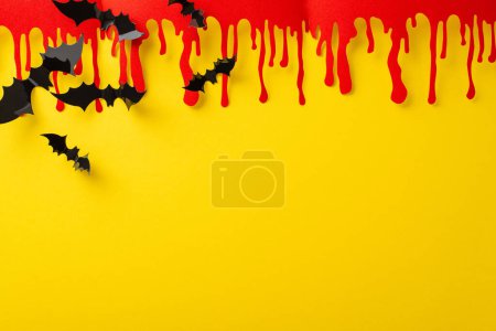Imaginative Halloween idea. Top view of thematic decorations, eerie blood smears and bats on yellow backdrop, blank space for text