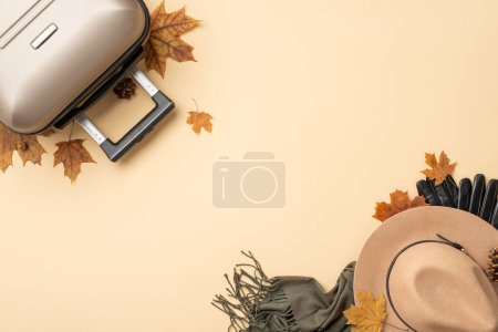 Téléchargez les photos : Voyage d'automne rêves. Une prise de vue aérienne mettant en valeur une valise grise, des feuilles d'érable, un chapeau en feutre serré, une écharpe et des gants disposés sur un fond isolé beige, idéal pour vos besoins promotionnels ou textuels - en image libre de droit