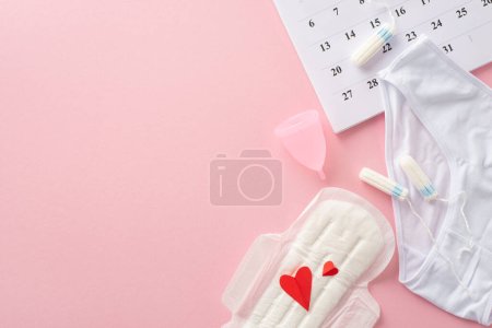 Artículos de higiene femenina como almohadilla con corazones rojos, simbolizando sangre, tampones, copa menstrual, calzoncillos, calendario que marca el inicio del ciclo, sobre un fondo rosa pastel con espacio para texto o marca