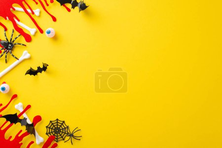 Creative Halloween arrangement. Top view shot of themed embellishments, chilling blood streaks, bones, eyeballs, creepy crawlies, spiders, cobweb, bats on yellow backdrop, space for text insertion