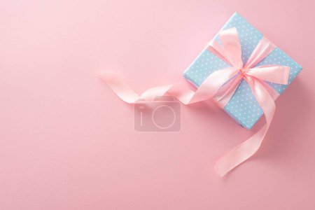 Téléchargez les photos : Cette scène de félicitations présente une vue de dessus d'un coffret cadeau bleu pastel orné de pois et d'un adorable ruban rose, le tout sur un fond rose pastel - en image libre de droit