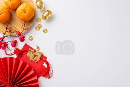 Photo for Chinese New Year festivity concept. Top view of traditional coins, decorative fan, plate with mandarin oranges, golden sycee, intricate paper cutouts on festive white backdrop with space for greetings - Royalty Free Image