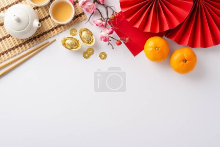Photo for Unveil beauty of Chinese New Year through lavish table arrangement. Top view of intricate fans, green tea ceremony essentials, Feng Shui accents, fresh tangerines, sakura blossoms on white backdrop - Royalty Free Image