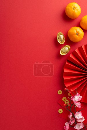 Photo for Elements of joy in Chinese New Year. Overhead vertical shot including fan, feng shui essentials, traditional coins, sycee, Hong Bao packets, fruits, sakura on red background with text-friendly area - Royalty Free Image