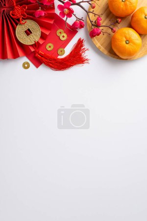 Photo for Celebrate Chinese New Year's vibrancy through this top view vertical composition showcasing fan, Hong Bao, lucky coin charm wall hanging, tangerines on white neutral background with sakura accents - Royalty Free Image