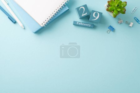 Téléchargez les photos : Dernier jour de travail du mois de février capturé : photo panoramique avec tampons, stylos, accessoires de bureau, une petite plante et un bloc de date pour le 29 février, sur une surface bleue douce, laissant de la place pour le libellé - en image libre de droit