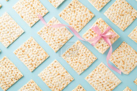 Passover tradition captured: top view of an array of neatly arranged matza, with one distinctively wrapped in a pink ribbon bow, presented on a soft blue backdrop