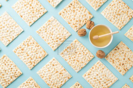 Passover theme design. Overhead shot showcasing neatly arranged matza, walnuts, and a bowl of honey with a wooden spoon, all set against a soft blue backdrop