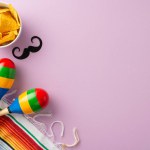 Celebrate Cinco de Mayo with a vibrant top view of festive items: colorful sombrero, maracas, mustache, a bright serape, and a bowl of nachos, on a soft purple backdrop
